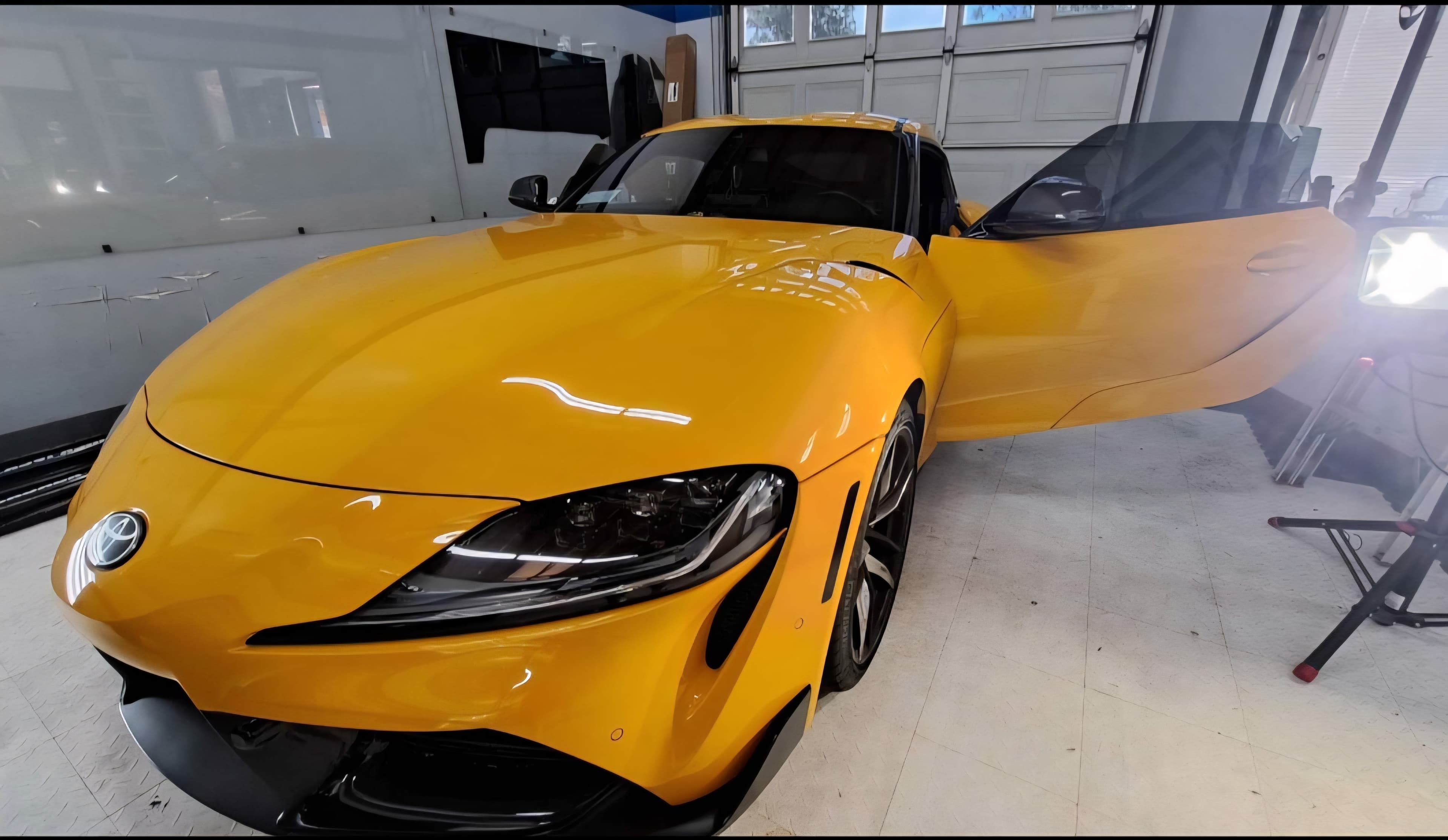 Bright yellow Toyota Supra with an open door parked inside a professional auto garage.
