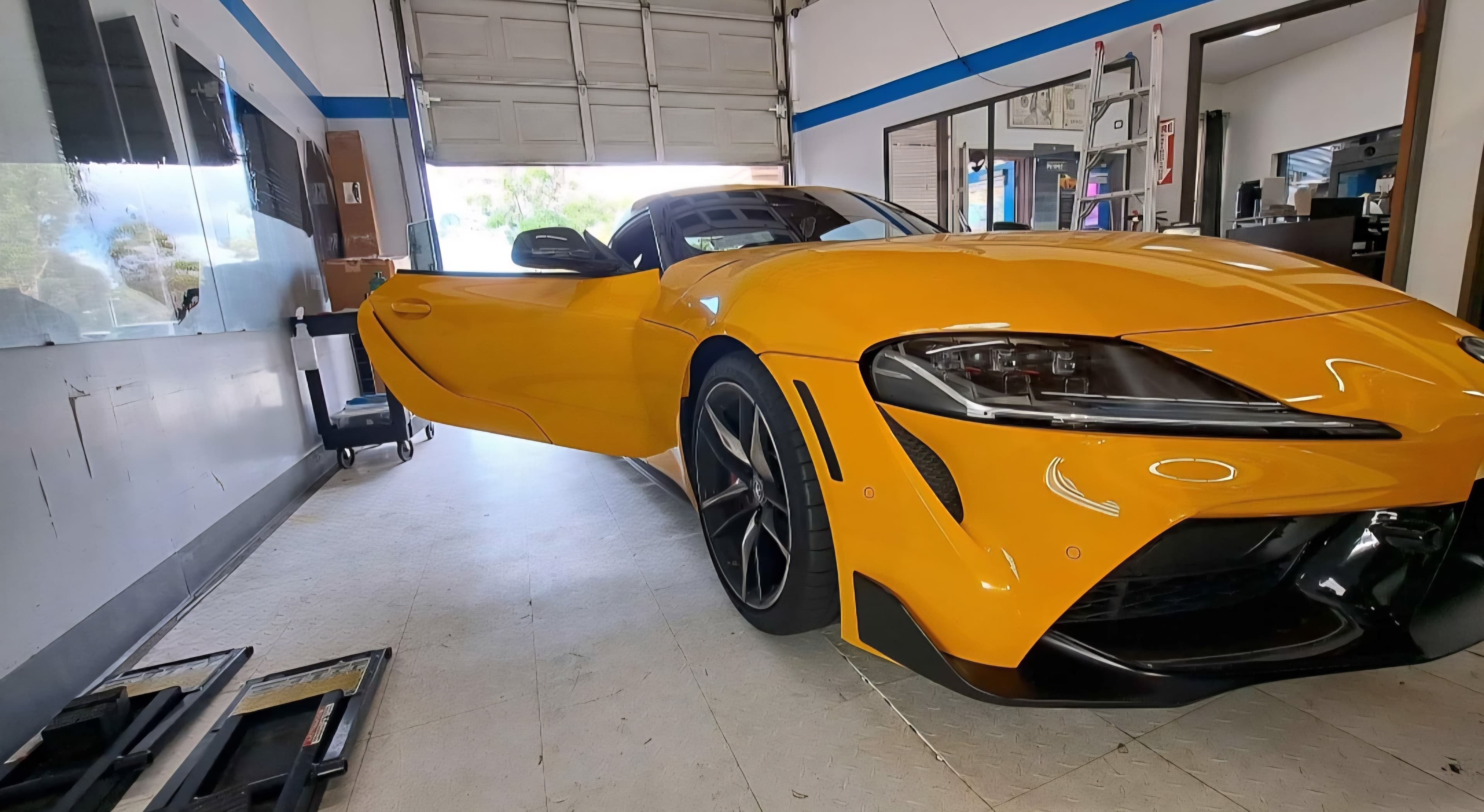 Bright yellow sports car with the driver-side door open inside a professional auto shop.
