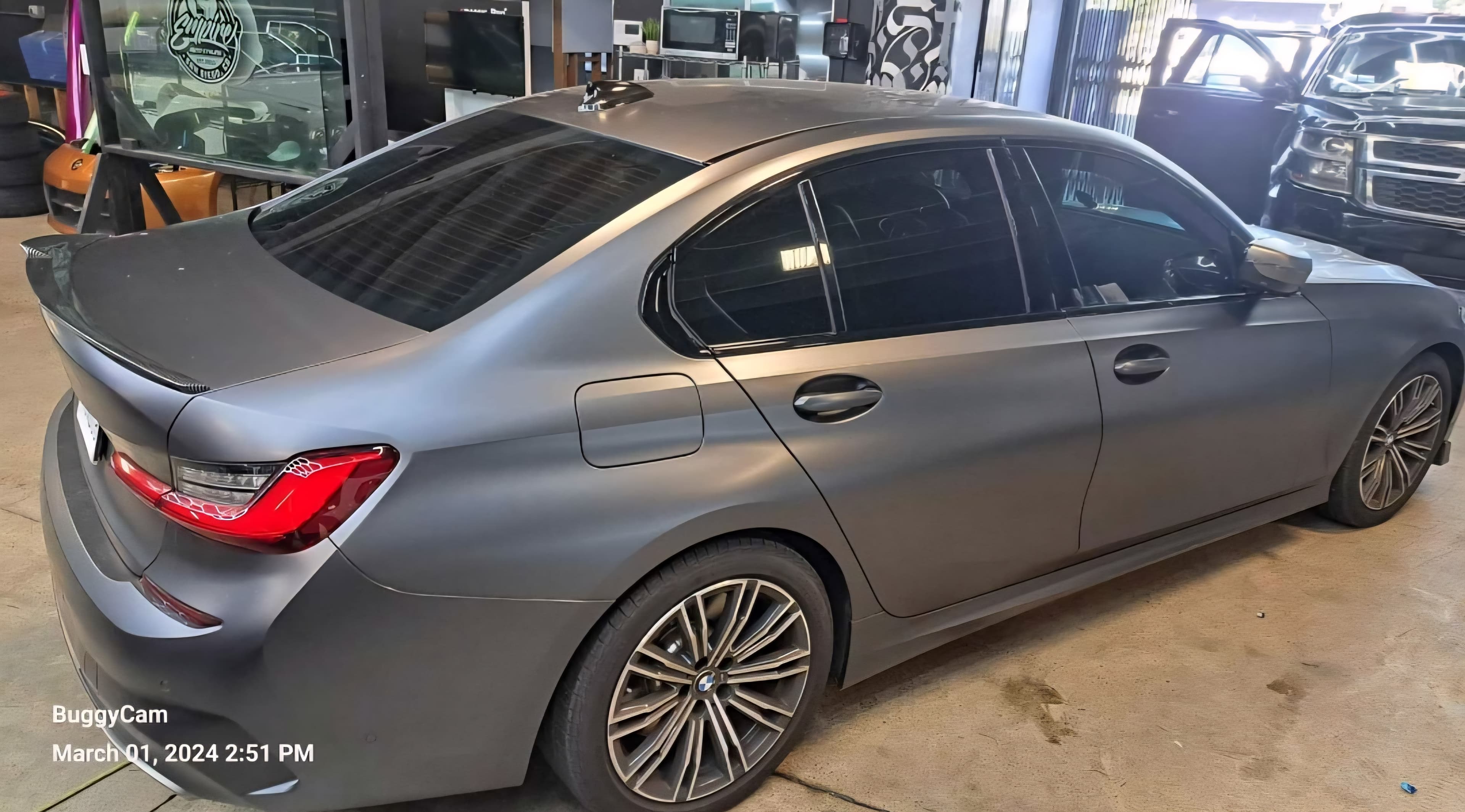 Matte grey BMW sedan with tinted windows and multi-spoke wheels parked in a detailing shop.