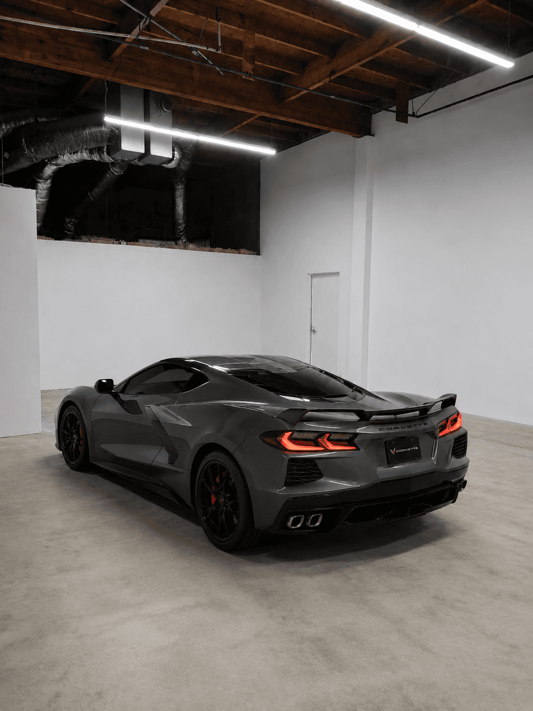 Dark gray Chevrolet Corvette C8 with glowing red taillights in a minimalist white studio.
