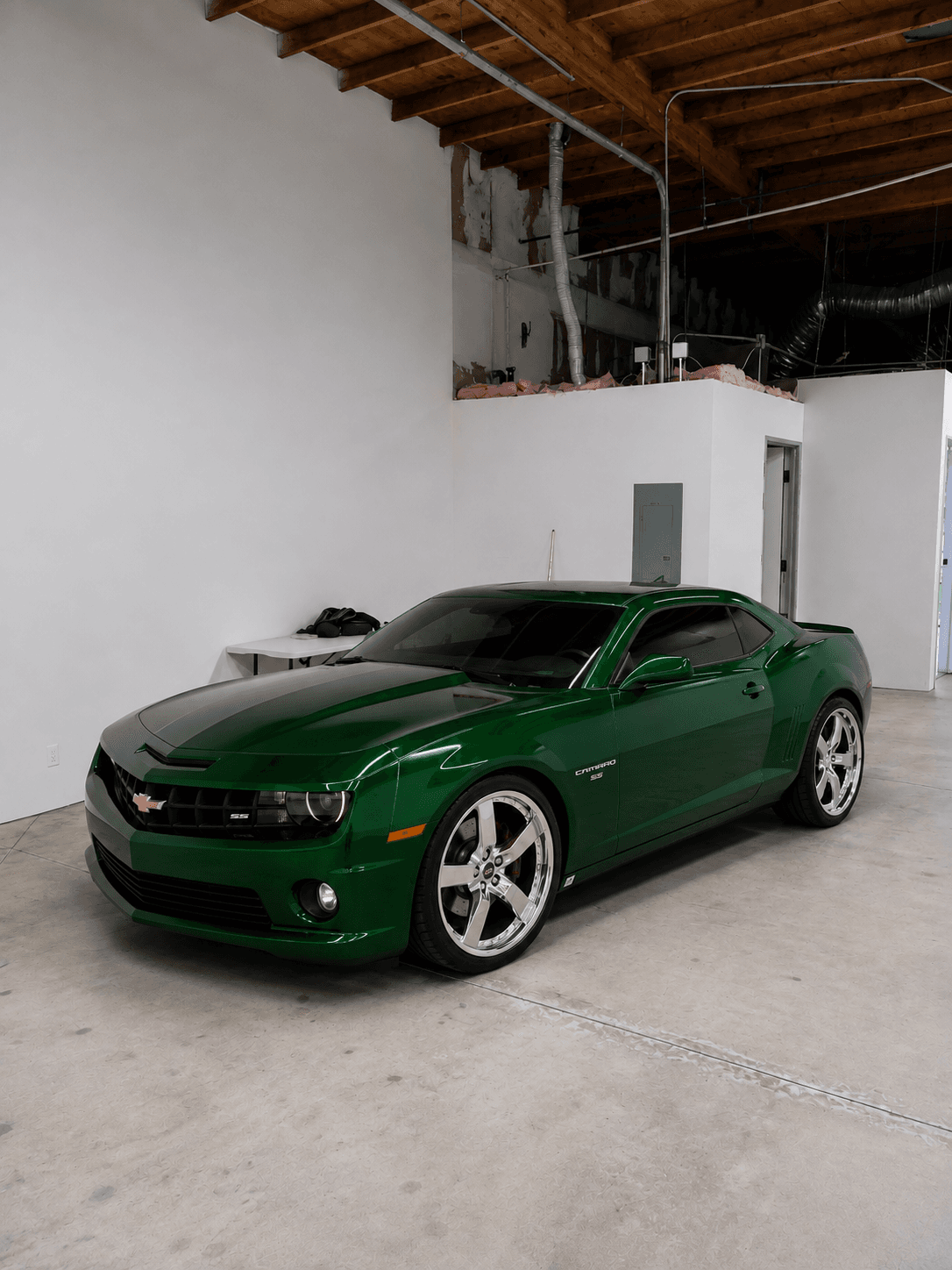 Metallic green Chevrolet Camaro SS with chrome wheels parked in a minimalist white walled garage.