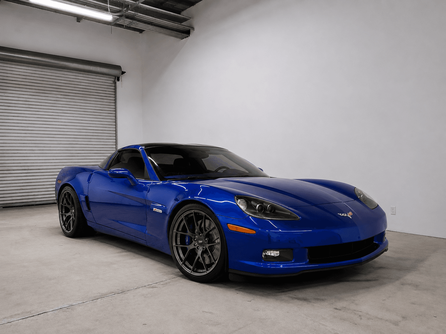 Sleek blue Chevrolet Corvette Z06 with dark wheels parked inside a minimalist white walled garage.